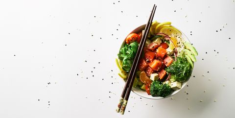 poke bowl with salmon, avocado, cucumber, arugula, broccoli, rice, carrot and sweet onions with chuka salad, chopsticks isolated over white background. top view