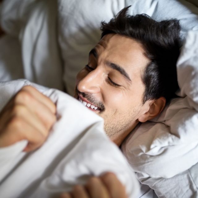 smiling young man sleeping comfortably in bed at home