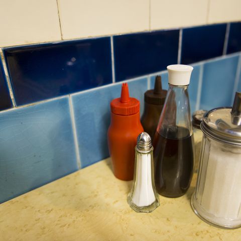 a close up of salt and sugar shaker, bottle of vinegar, tomato ketchup and brown sauce condiments on a cafe table london, uk