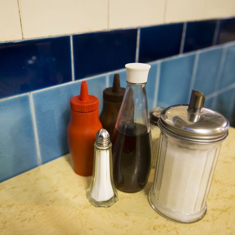 a close up of salt and sugar shaker, bottle of vinegar, tomato ketchup and brown sauce condiments on a cafe table london, uk