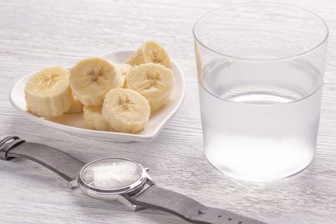 sliced and whole bananas on a white plate on the old wooden table misted up with clear water wristwatches for diet planning the concept of healthy eating
