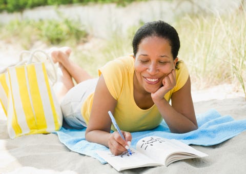 black woman doing crossword puzzle on beach