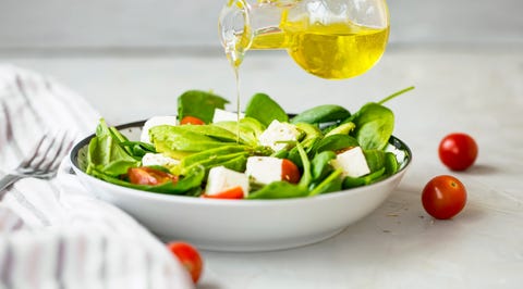 Pouring olive oil in healthy green vegetables and cheese salad, healthy eating mediterran diet concept, feta cheese and avocado salad with spinach , tomatoes and lettuce bowl with olive oil bottle