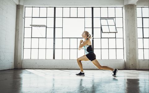 Side view of young woman in gym doing lunge