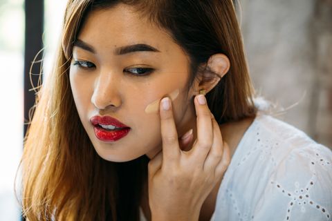 closeup young asian woman with red lips applying corrector on face on blurred background