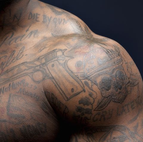 african american mans shoulder and chest view with tattoos of gun, skull, and different phrases