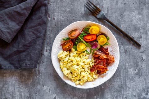 Scrambled eggs with fried bacon and salad with tomato, low carb, from above