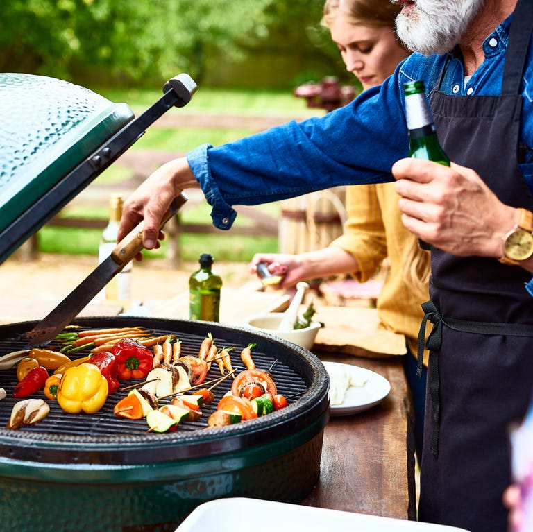 Man using tongues to turn vegetables on bbq