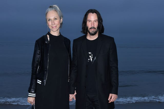 Keanu Reeves et Alexandra Grant se tiennent la main sur la plage, posant pour les caméras.