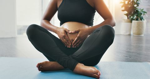 shot of an unrecognizable pregnant woman holding her belly while sitting down on a yoga mat