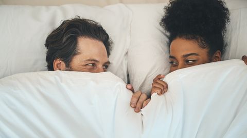 man en vrouw liggen onder witte deken en kijken elkaar aan