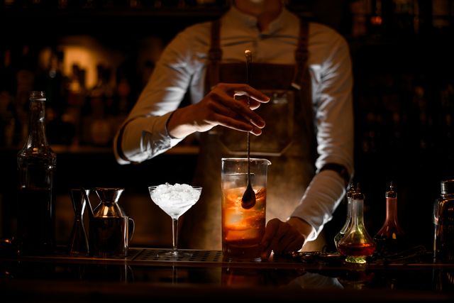 male bartender in white shirt and leather apron stirring alcohol cocktail with a special bar spoon