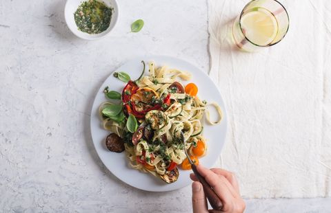 Eating Fettucine with roasted colorful vegetables and parsley  pesto