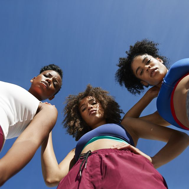 directly below portrait of confident female friends in sportswear standing against blue sky on sunny day