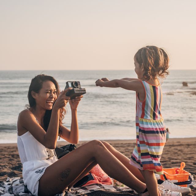 two people, mother and daughter relaxing on the beach, mother is taking pictures with instant camera