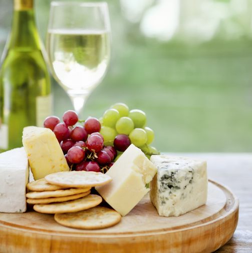 a lovely cheese board with grapes and white wine sitting on a table  natural lighting with a backyardgarden setting in the background