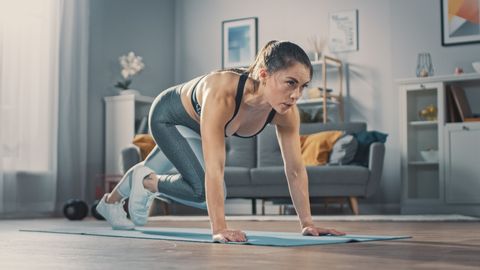 shot of a beautiful confident strong fitness female in a grey athletic outfit is doing mountain climber exercises in her bright and spacious apartment with cozy minimalistic interior