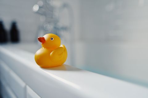 bright yellow toy rubber duck sitting on the side of a white bath