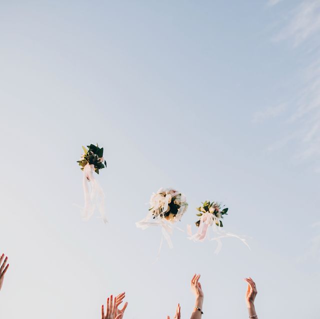 bride and bridesmaids throwing wedding bouquets up in the sky in evening soft light stylish wedding bouquets with ribbons in sky happy moment