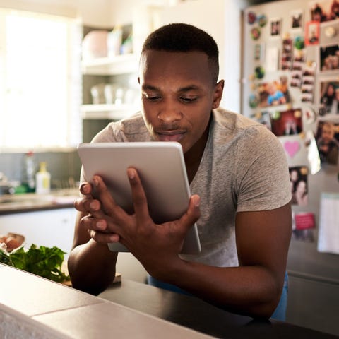 I need to find some good cooking videos cropped shot of a handsome young man using a digital tablet while making breakfast in his kitchen at home