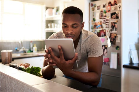 cropped shot of a handsome young man using a digital tablet while making breakfast in his kitchen at home