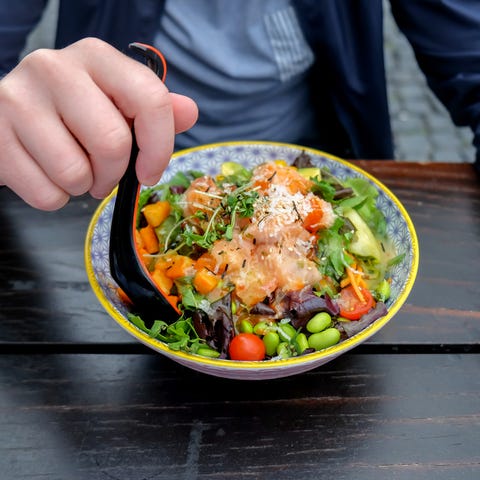 close up one young man eating healthy poke bowl, sitting alone outside a sidewalk café