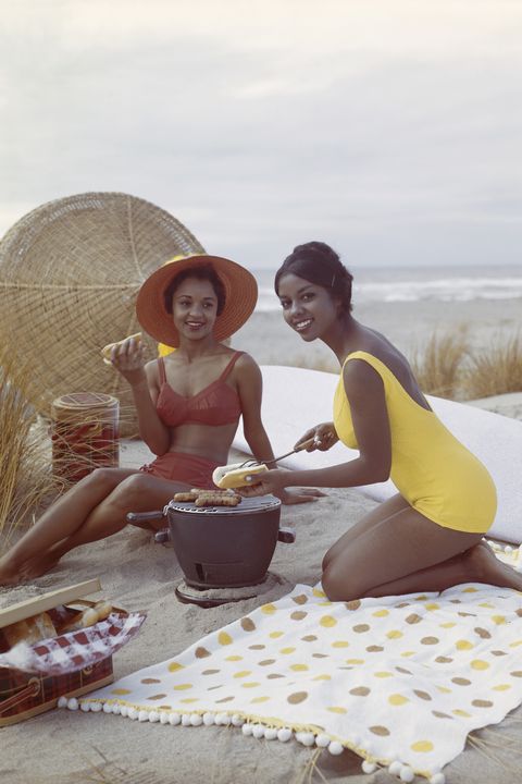 young women holding hot dog on beach, smiling