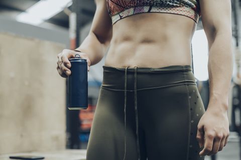 unknown strong woman holding blue can after training she is wearing a colorful top and green leggins she is in a gym