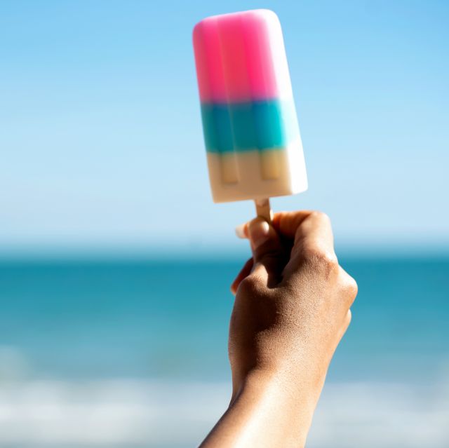 cropped image of womans hand holding ice cream by the sea against clear blue sky