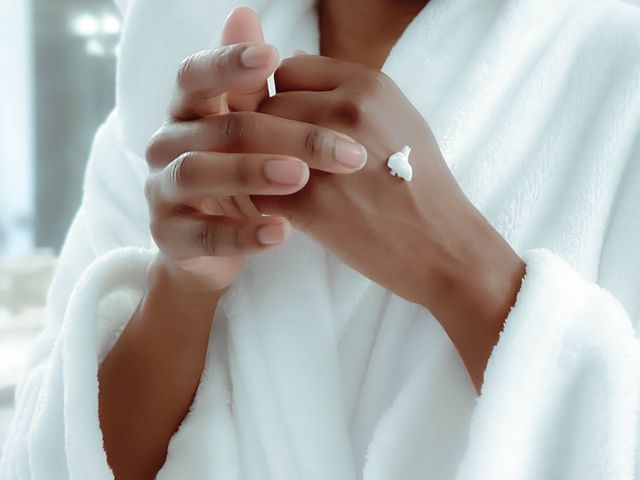 mid adult black woman in bathrobe after morning shower moisturizes her skin