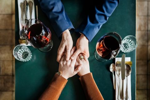 an aerial view of a couple holding hands and drinking red wine while sitting at a restaurant table for lunch together