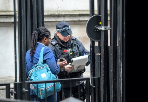 Metropolitan police officer checking the pass of a woman as she waits at the security gates outside the Prime Ministers Downing Street offices , Westminster, London, UK uk criminal justice system stop and search