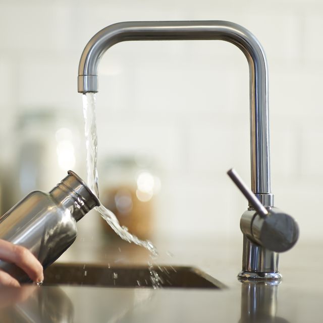 a woman cleans a plastic free and reusable water bottle in a kitchen sink, close up