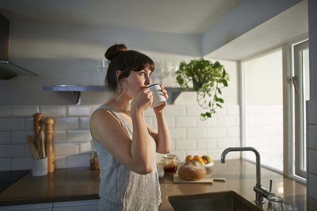 une femme debout dans sa cuisine boit dans une tasse