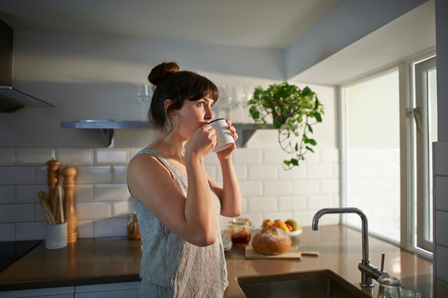 une femme debout dans sa cuisine boit dans une tasse