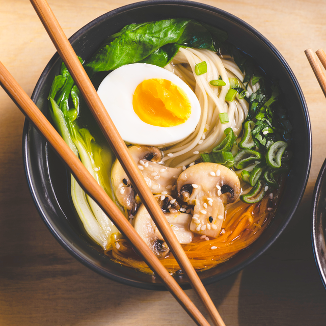 traditional japanese ramen soup with  mushrooms, bok choy, greens in  two black bowls on the orange background, top view, close up