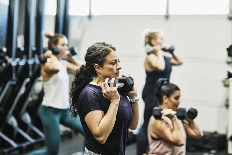 woman doing dumbbell squats during fitness class in gym