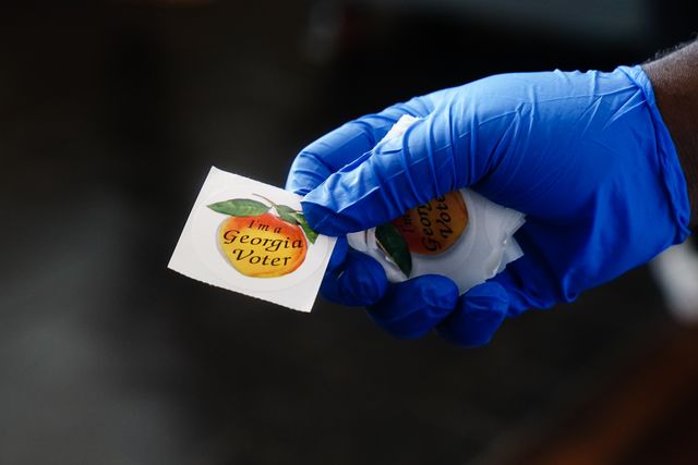 atlanta, ga   june 09 a polling place worker holds an im a georgia voter sticker to hand to a voter on june 9, 2020 in atlanta, georgia georgia, west virginia, south carolina, north dakota, and nevada are holding primaries amid the coroanvirus pandemic photo by  elijah nouvelagegetty images