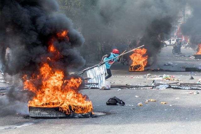 a person drags items into the street near burning barricades as opponents of haitian president jovenel moise demonstrate on january 15, 2021 in port au prince to demand his departure from power on february 7, the day they believe to be the last of his term   several hundred demonstrators made their way through the city, they set barricades made of burning tires or garbage, paralysing traffic and stressing parents who, picking up their children as school let out, were walking or riding on motorcycles with their children in school uniforms photo by valerie baeriswyl  afp photo by valerie baeriswylafp via getty images