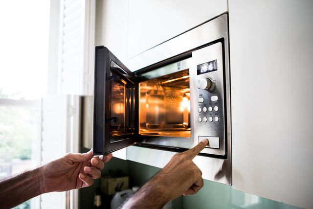 a man using a microwave oven his finger on the opening button