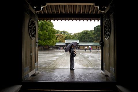 a young woman with an umbrella standing in a large japanese traditional doorway at the meiji shrine