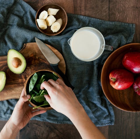 flat lay shot of female hands preparing vegetarian meal, picking baby spinach with various raw ingredients on a wooden worktop