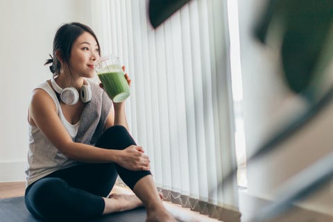 beautiful young asian woman in sportswear drinking protein shake after exercise, relaxing at home