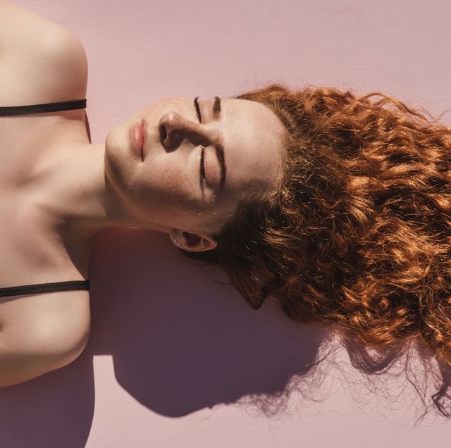 curly red haired girl with closed eyes upside down on pink background