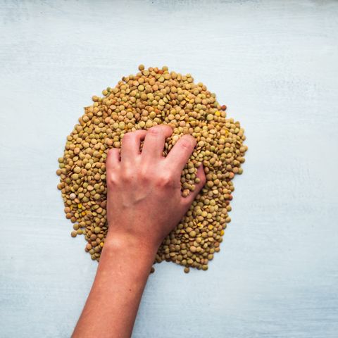 womans hand holding a handful of peas on a white background