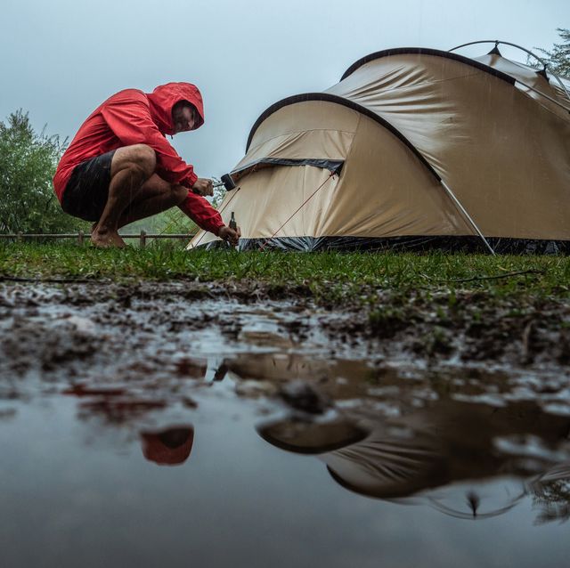 man camping fixing tent on rainy day