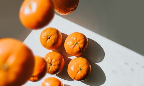 shiny bright mandarin oranges sit on a clean white shadowy surface while others fall from above creating shadows space for copy