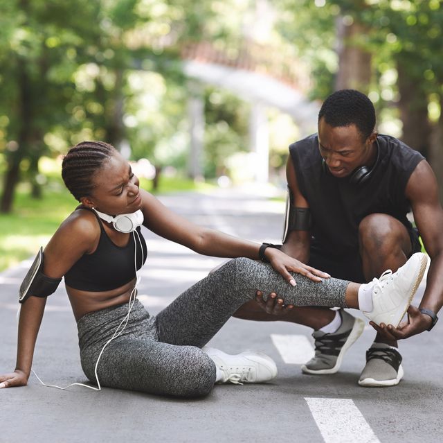 caring black man massaging injured leg of girlfriend after running together outdoors, free space