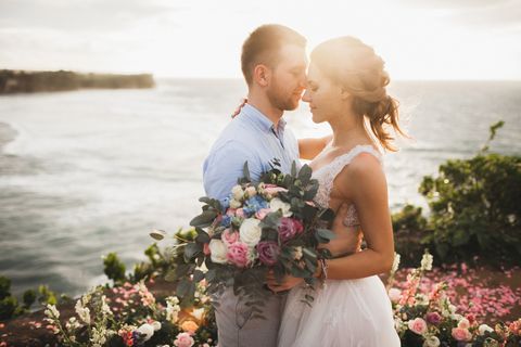 sunset wedding ceremony outdoors in bali young couple kissing in love sensual and tender bride and groom beautiful flower arrangement for celebration honeymoon for two warm orange sunshine destination tropical summer wedding on balangan beach, indonesia