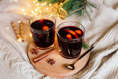 two glasses with hot winter drink mulled wine with orange slices, spices and knitted white christmas background